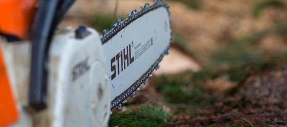 Extreme close up of STIHL chainsaw burry wooded background